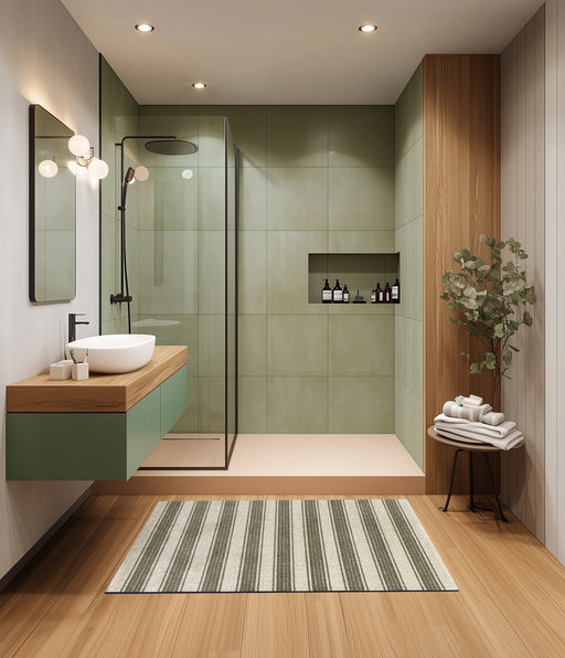 Modern bathroom with green tiles, wooden vanity, and striped rug.